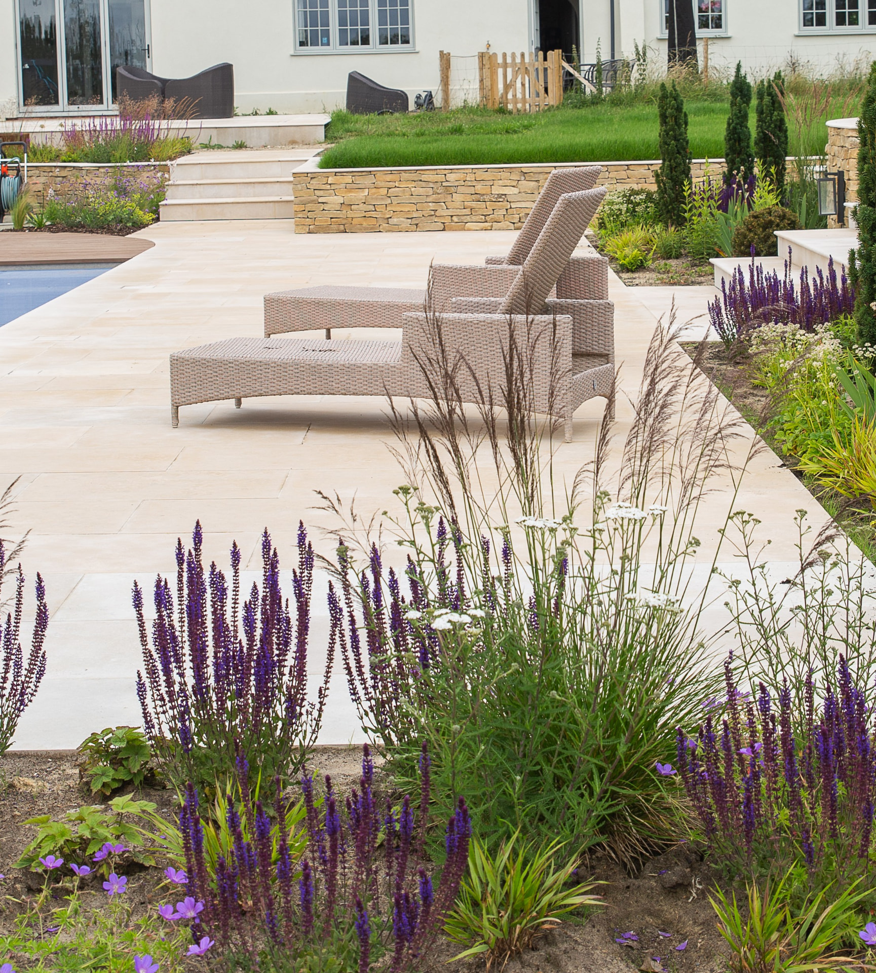 A refined limestone patio with planted borders and garden loungers beside a pool